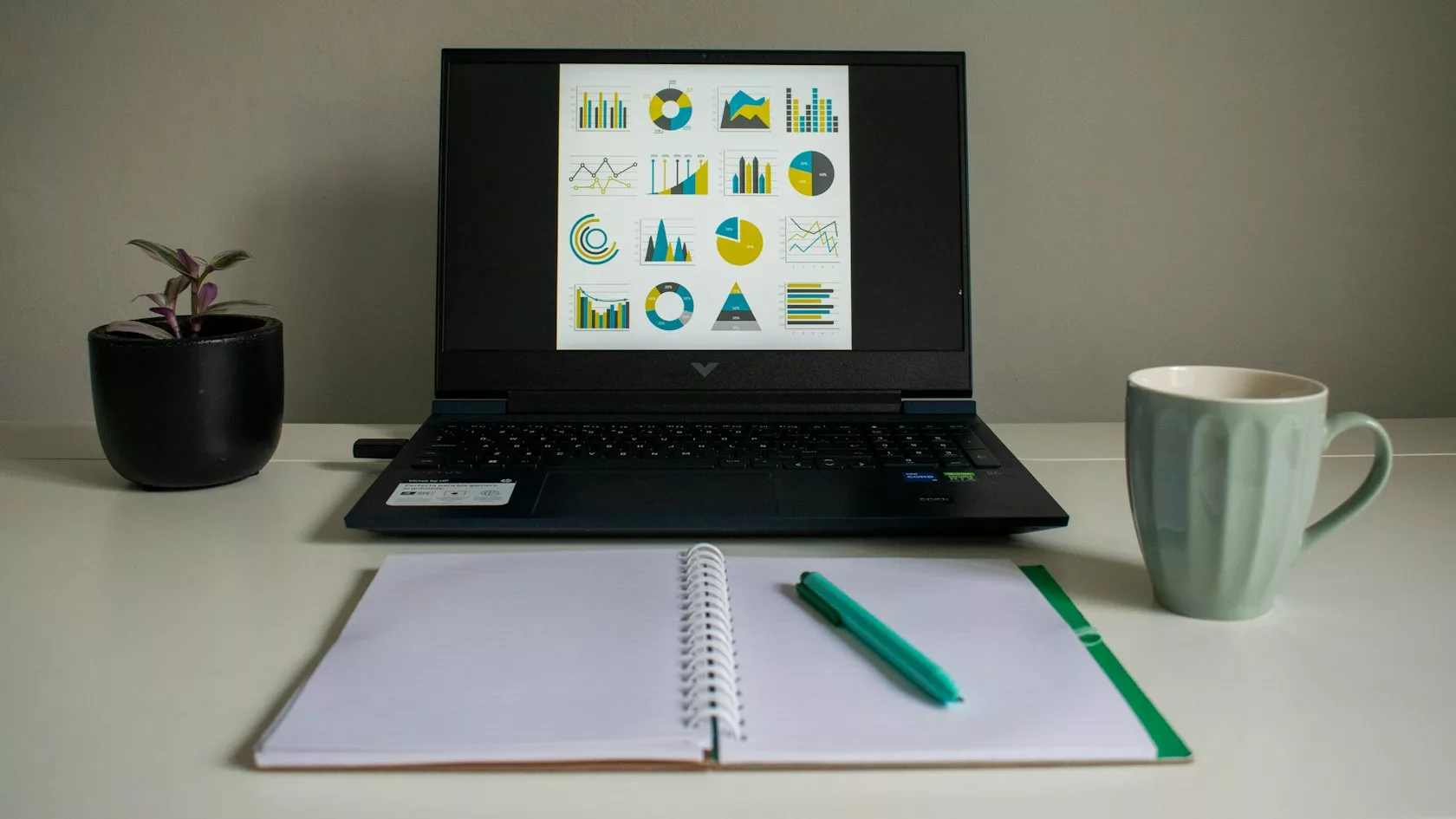 Portátil con gráficos de análisis de datos junto a una libreta y una taza