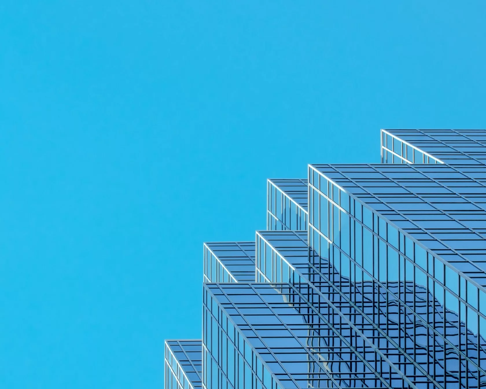 Edificio moderno de cristal con fachada escalonada reflejando un cielo azul